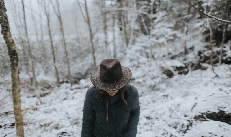 A woman in hat, coat and gloves walks in a snowy forest.