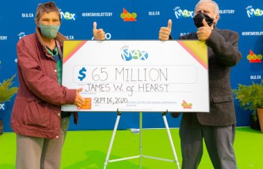 Le couple gagnant en train de tenir leur chèque de 65 millions avec un pouce en l'air
