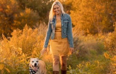 A picture of Jessica Forgues walking in a field with her dog, wearing a yellow dress and boots.