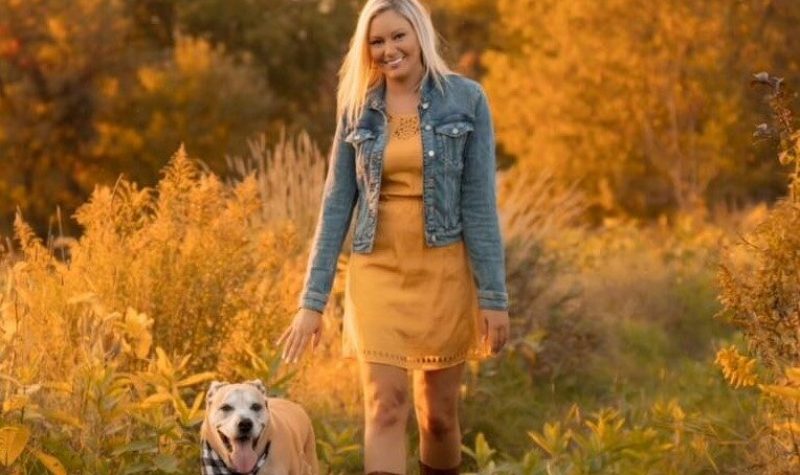 A picture of Jessica Forgues walking in a field with her dog, wearing a yellow dress and boots.