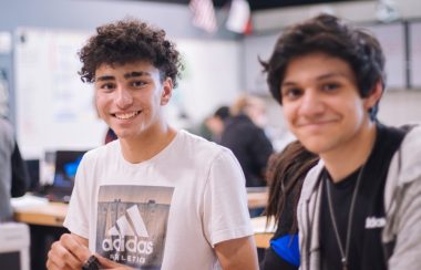 Two male students in a classroom smile at the camera.