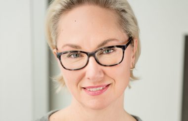 A close-up head shot of Jade Savage standing in front of a white background.