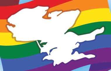 A white outline of the Prince Edward County landmass superimposed over a stylized Pride flag with six horizontal solid (red, orange, yellow, green, blue, and purple) coloured bars.