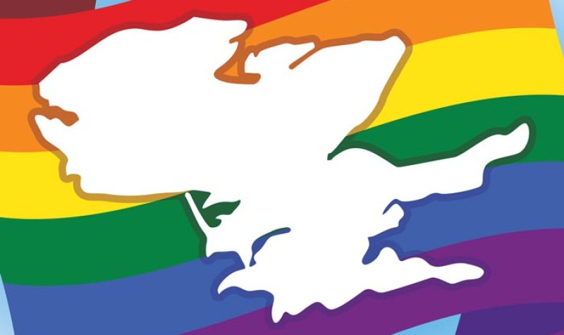A white outline of the Prince Edward County landmass superimposed over a stylized Pride flag with six horizontal solid (red, orange, yellow, green, blue, and purple) coloured bars.