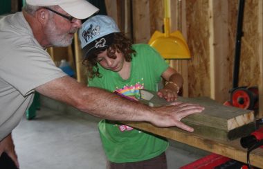 Danny and his grand-daughter are in his workshop cutting a piece of wood.