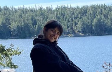 Smiling woman outside with forest and lake in background