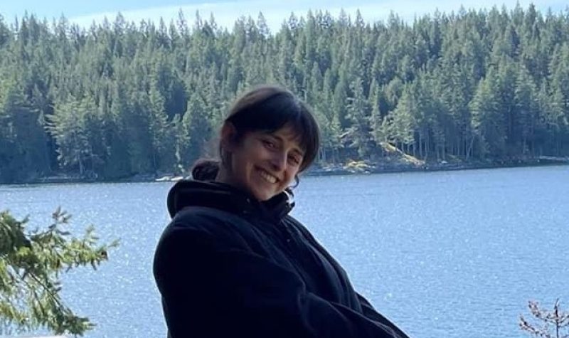 Smiling woman outside with forest and lake in background