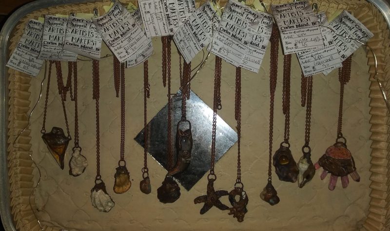 A dozen necklaces with elecroform copper pendants hang in an old suitcase.