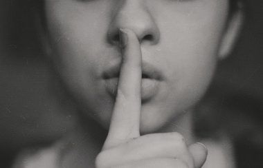 A woman holds a finger in front of her mouth