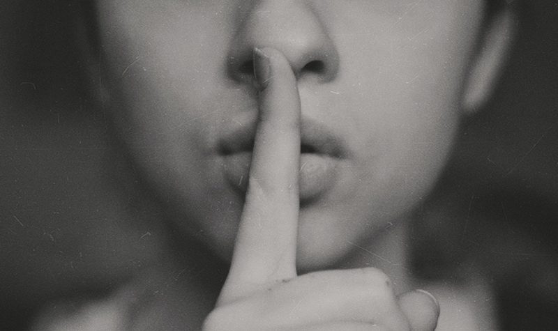 A woman holds a finger in front of her mouth