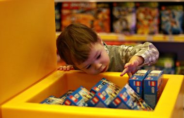 Jeune enfant découvrant des boites de jeux dans une caisse de rangement jaune.