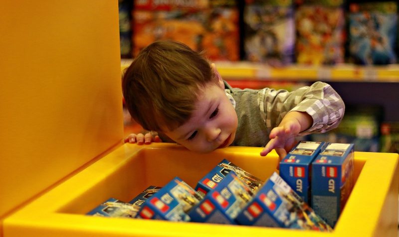 Jeune enfant découvrant des boites de jeux dans une caisse de rangement jaune.