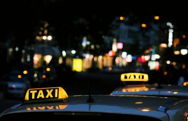 the light of two taxi signs are lit yellow on top of two cars in a night scene in a city.