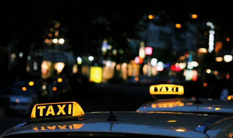 the light of two taxi signs are lit yellow on top of two cars in a night scene in a city.