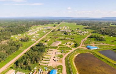 Little Red River Cree Nation from a helicopter perspective. The grass and trees below are green, aren't any cars on the road, and the weather is clear.