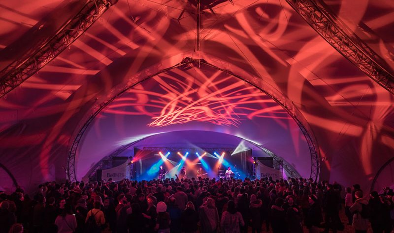 L'intérieur d'une grande tente, des lumières rouges et bleus illuminent l'estrade lors d'un concert live.