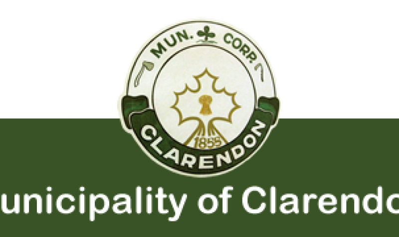 The logo of the municipality of Clarendon, featuring a green and white background with a clover leaf, an ax and a scythe surrounding a maple leaf.