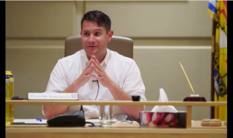 A man in a white shirt sitting at a council desk with hands together in front of him.