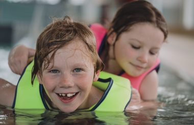 On aperçoit deux enfants portant des gilets de sauvetage et qui sourient en jouant dans l'eau
