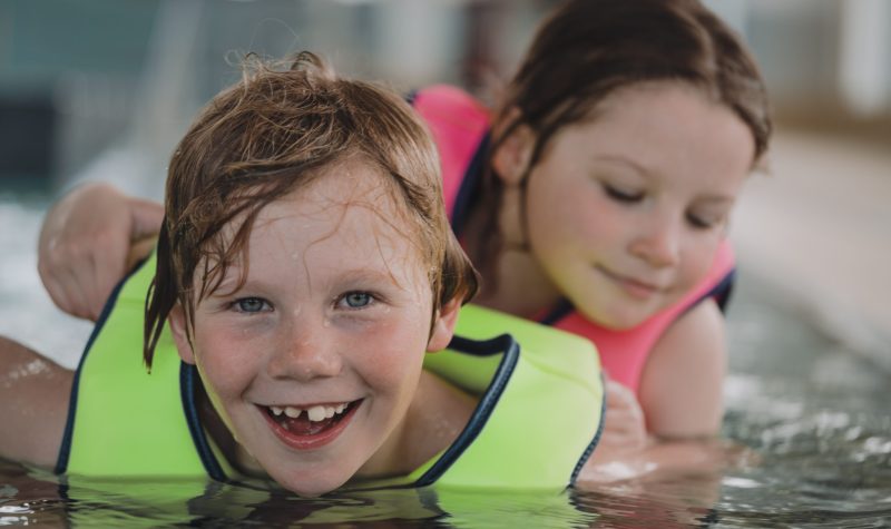 On aperçoit deux enfants portant des gilets de sauvetage et qui sourient en jouant dans l'eau