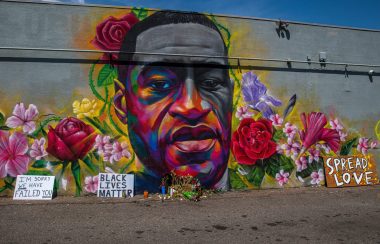 A mural of a man's face surrounded by colourful flowers on a grey concrete background