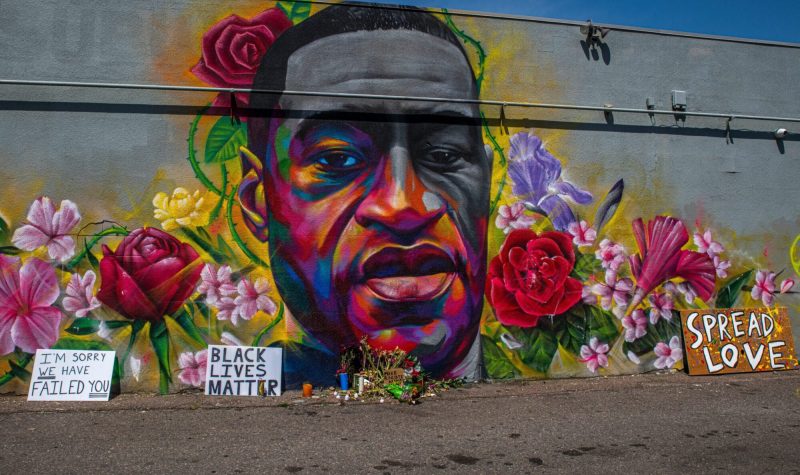 A mural of a man's face surrounded by colourful flowers on a grey concrete background