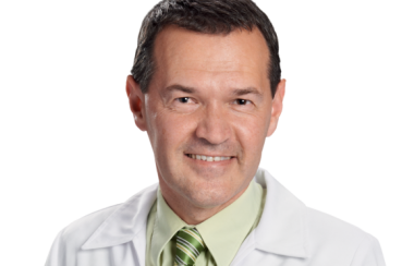 A headshot of pharmacist Marc Aufranc wearing a green dress shirt and tie under a white collared jacket.