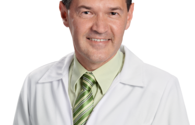 A photo of pharmacist Marc Aufranc on a blank background, wearing a white lab coat and a green shirt and tie.