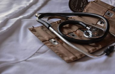 A stethoscope lies atop a leather case and white sheet.