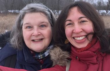 Two women stand side by side smiling on a field.