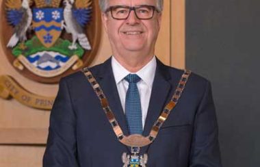An image of Mayor Lyn Hall standing in front of the City of Prince George crest.