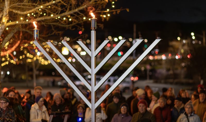 A giant Menorah with two flames in the foreground with a blurred out crowd in the background.