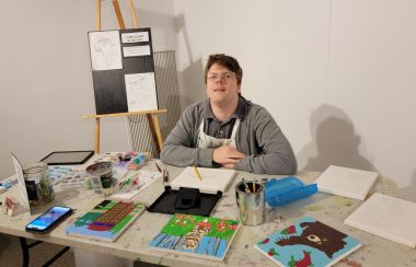 A man sitting at a table with a collection of art and art supplies