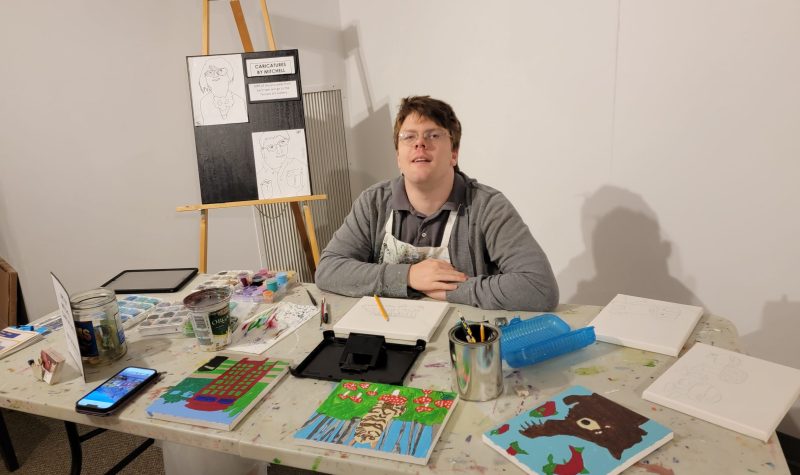 A man sitting at a table with a collection of art and art supplies