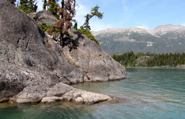 a rocky turn on the Morice River shows aquamarine water, blue skies, and a view of the Babine Mountain range in the distance.