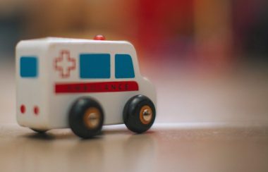 On voit une ambulance jouet en premier plan, placé sur une table. L'arrière plan de la photo est flou.