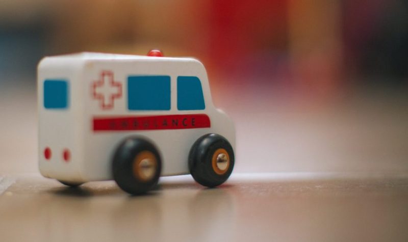 On voit une ambulance jouet en premier plan, placé sur une table. L'arrière plan de la photo est flou.