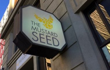 Mustard Seed logo on the side of a building. Weather is clear.