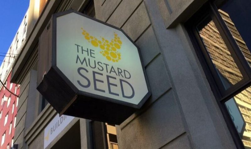 Mustard Seed logo on the side of a building. Weather is clear.