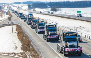 Multiple trucks with red and white banners reading out FREEDOM on their front grills. The trucks are in single formation on a highway.