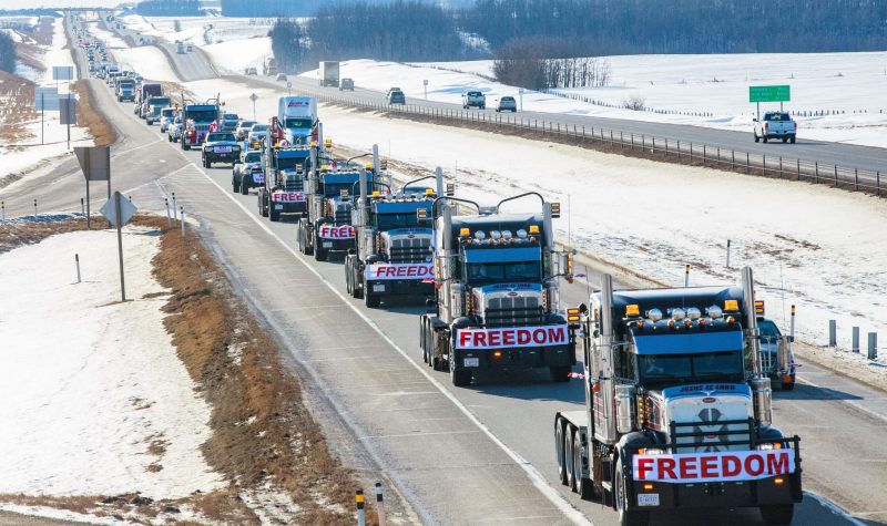 Multiple trucks with red and white banners reading out FREEDOM on their front grills. The trucks are in single formation on a highway.