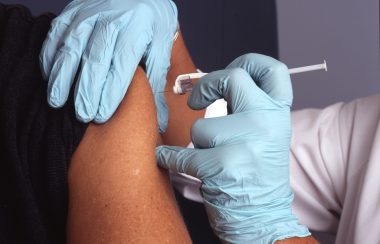 A person with blue gloves giving a needle to another person's arm.