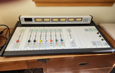 An audio mixing console sits on a desk