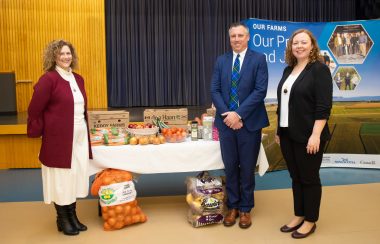 Photo of Janet Simm, CEO & President of Northwood, Agriculture Minister Greg Morrow, and Letitia Rowley from Gordon Food Services. There is a table of produce behind them. They are all standing and smiling for the camera.