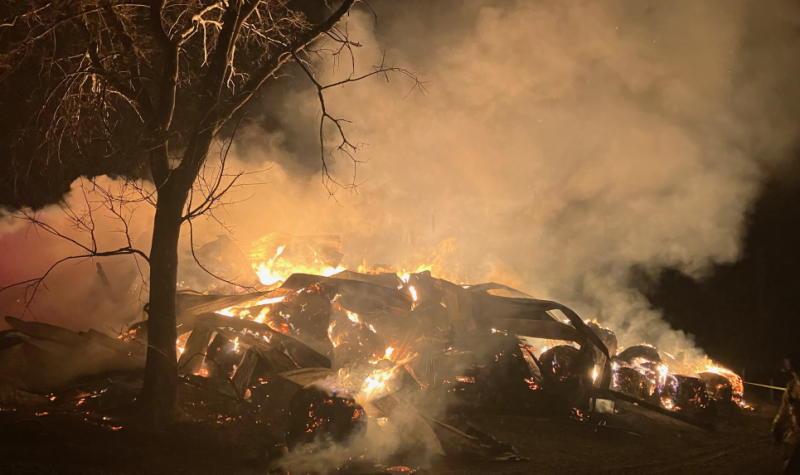 At nighttime a pile of burning debris glows orange after a barn used for feed and equipment storage burned to the ground.