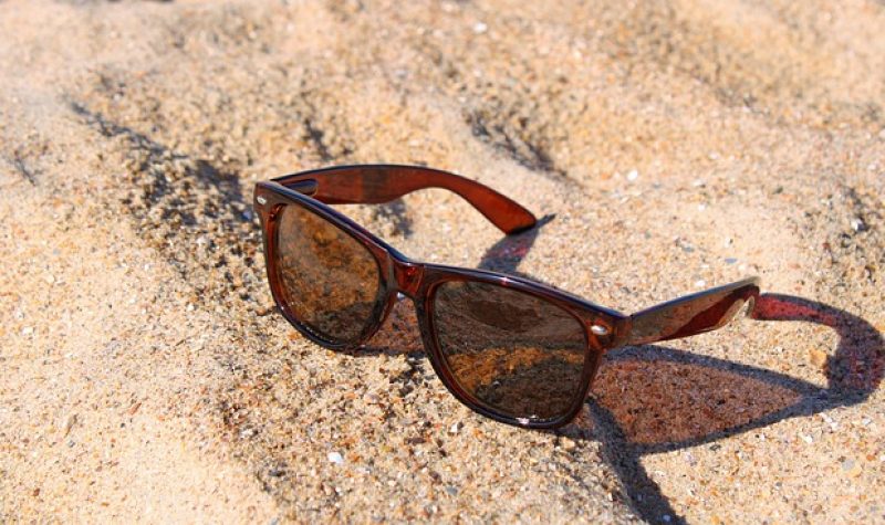 Une paire de lunette soleil repose sur le sable.
