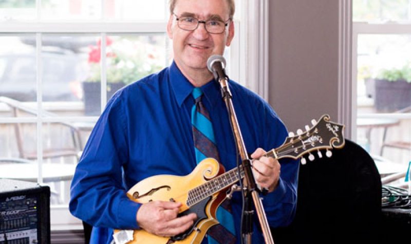 Un homme portnt une chemise bleu et jouant de la mandoline.