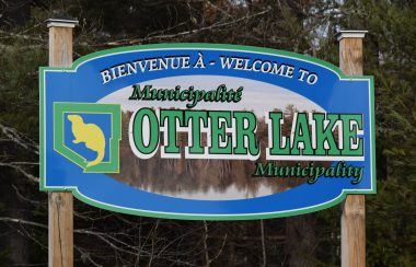 The sign for Otter Lake Quebec, blue with green letters and a yellow otter silhouette.