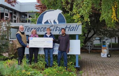 Four people stand holding a large cheque in front of a sign that says Terrace City Hall