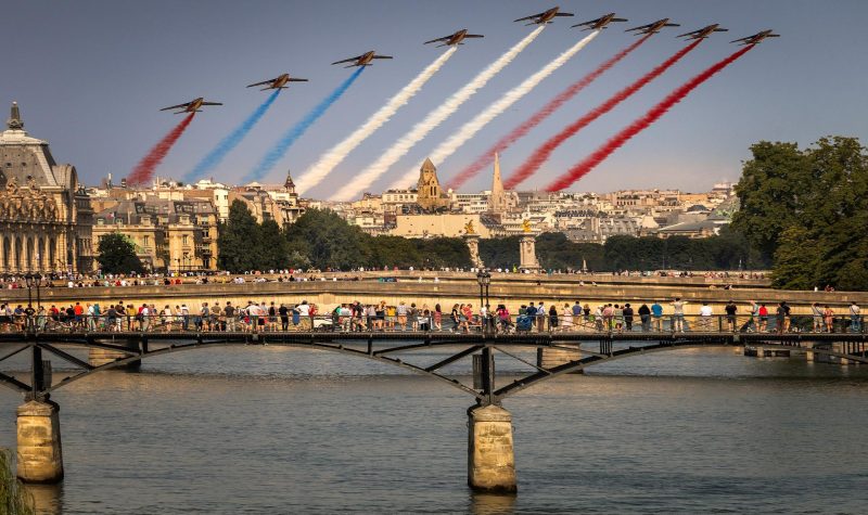 Un pont sur la seine a Paris au dessus duquel passe la patrouille de France, 9 avions lachant un panache de fumé bleu blanc rouge